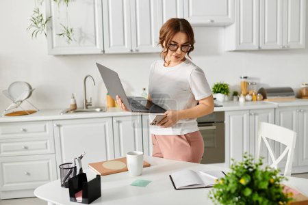 Photo for Middle-aged woman holding laptop in contemporary kitchen. - Royalty Free Image