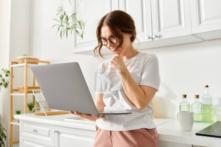 Middle aged woman uses laptop in kitchen.