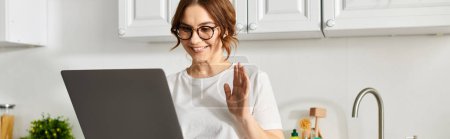 Photo for Middle-aged woman in glasses engrossed in laptop at home. - Royalty Free Image