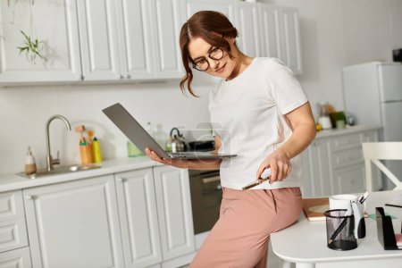 Middle-aged woman standing on kitchen counter, using laptop.