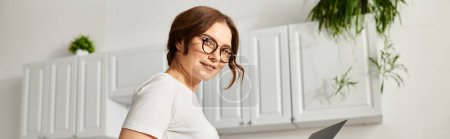 Photo for A middle-aged woman confidently holds a knife in a kitchen. - Royalty Free Image