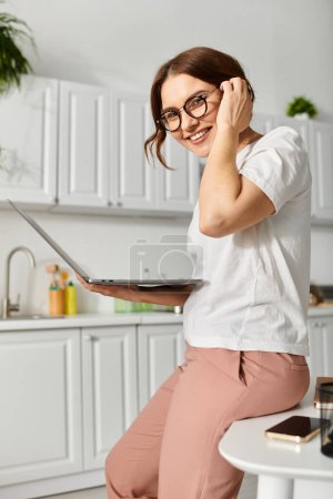 Femme d'âge moyen assise sur la table, travaillant sur un ordinateur portable.