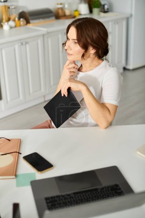 Frau mittleren Alters sitzt am Küchentisch und benutzt ein Tablet.