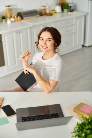 Belle femme d'âge moyen engagée dans le travail sur ordinateur portable à la table à la maison.