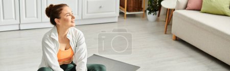 Foto de Mujer de mediana edad se sienta en la estera de yoga en la acogedora sala de estar. - Imagen libre de derechos