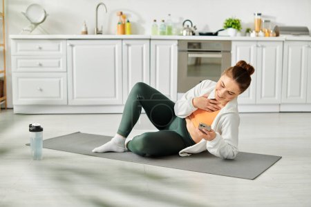 Middle-aged woman sitting on yoga mat, holding cell phone.