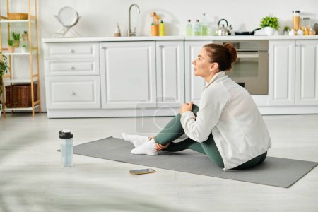 Middle aged woman peacefully practices yoga on her mat in a cozy kitchen.