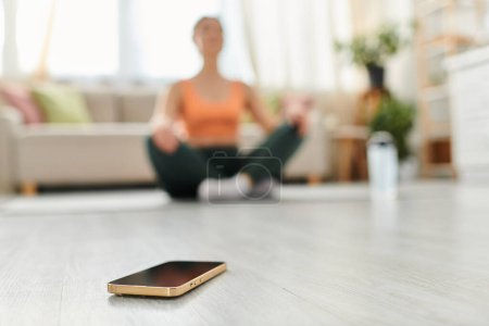 Foto de Una mujer de mediana edad se sienta en el suelo, enfocada en la pantalla de su teléfono celular. - Imagen libre de derechos