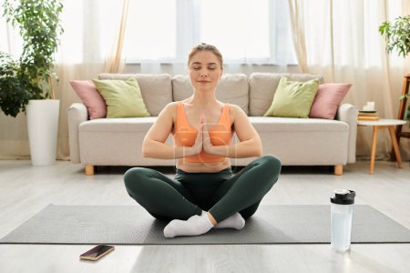 Middle-aged woman practices yoga in front of a sofa.