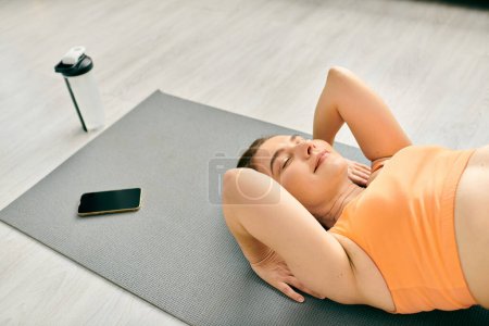 Middle-aged woman peacefully practices yoga on mat in gym.