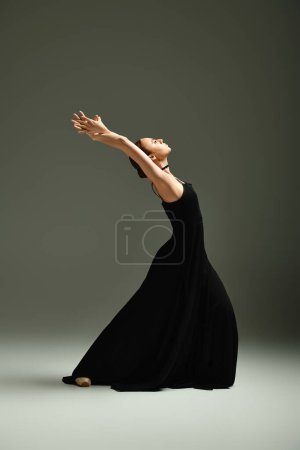 A young beautiful ballerina gracefully strikes a dance pose in a black dress.