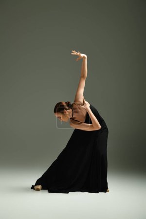 Jeune, belle ballerine en robe noire frappe une pose de danse avec grâce et habileté.