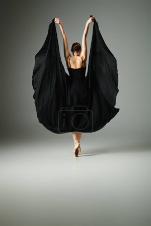A young, beautiful ballerina in a black dress dances gracefully.