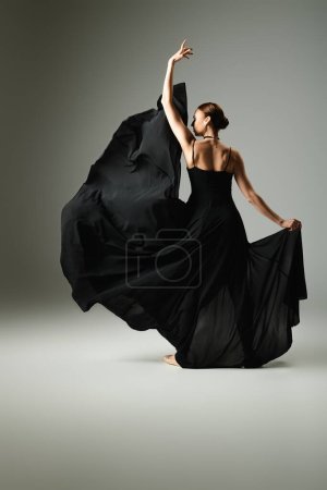 A young, beautiful ballerina in a black dress dances gracefully on stage.