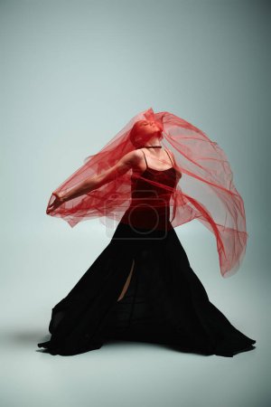 Una bailarina joven y hermosa en un vestido negro se mueve con gracia con un velo rojo que fluye.
