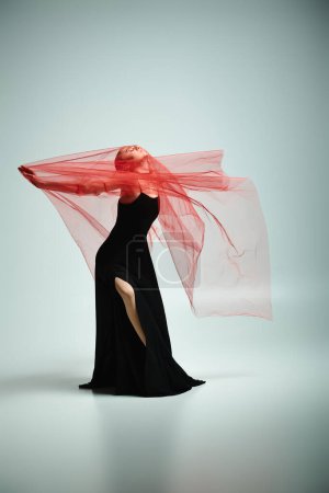 A young, talented ballerina gracefully dances in a black dress with a striking red veil.