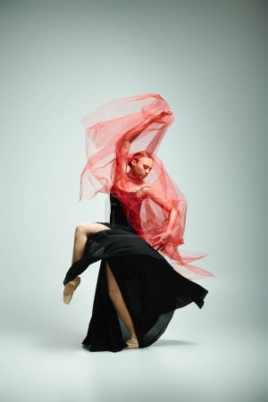 Téléchargez les photos : Une jeune femme en robe noire et une écharpe rouge dansent gracieusement. - en image libre de droit