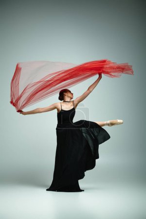 Une jeune ballerine en robe noire tient gracieusement une écharpe rouge vibrante.