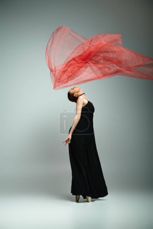 Graceful ballerina in black dress gracefully holds a vibrant red shawl.