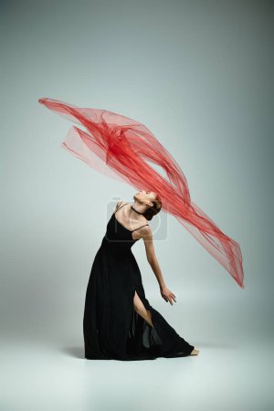 Photo for A young woman in a black dress gracefully holds a red veil. - Royalty Free Image