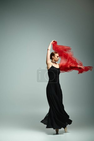 Foto de Una mujer en un vestido negro con gracia sostiene una bufanda roja vibrante. - Imagen libre de derechos