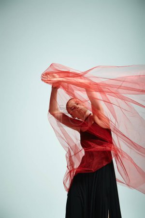 A young ballerina in a red top and black skirt gracefully dances in a talented performance.