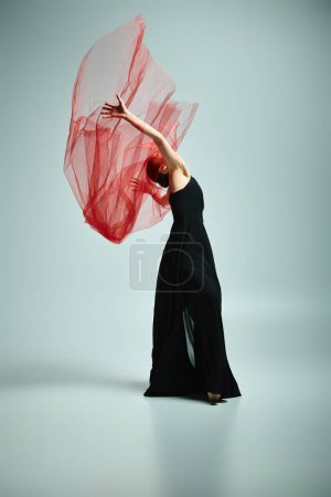 Una mujer con un vestido negro sostiene con gracia un velo rojo.
