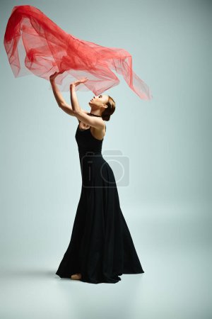 A young ballerina in a black dress gracefully holds a vibrant red scarf.