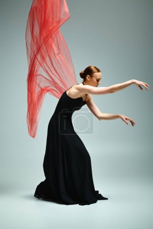 A young, beautiful ballerina in a black dress gracefully moves with a red veil.