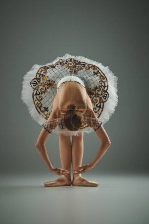 Foto de A young, beautiful ballerina in a white tutu is gracefully bending over. - Imagen libre de derechos