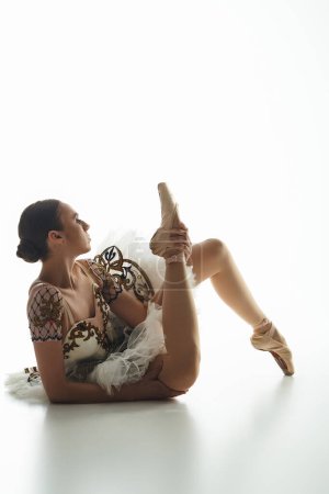 Una joven bailarina descansa graciosamente, sentada en el suelo con las piernas cruzadas.