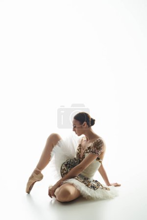 A young beautiful ballerina sits on the floor with crossed legs.