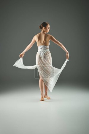 Una bailarina joven y hermosa baila con gracia en un vestido blanco que fluye.