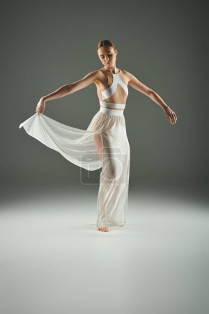 Young, beautiful ballerina in a white dress dancing gracefully on stage.