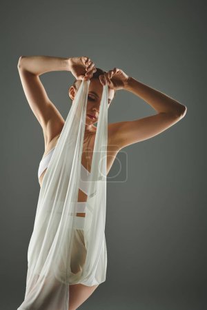 Foto de Young ballerina in white dress gracefully holds veil over head. - Imagen libre de derechos