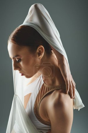 Young ballerina in white dress gracefully dances with a veil on her head.