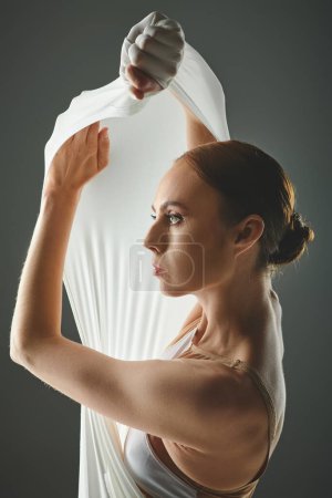 A young beautiful ballerina in a white dress gracefully holds a white veil.