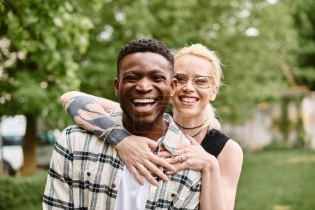 A joyful African American man holds a Caucasian woman in his arms, sharing a moment of love outdoors in a park.
