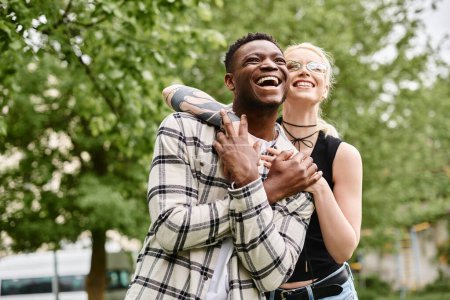 Ein glückliches multikulturelles Paar, ein afroamerikanischer Mann, der draußen in einem Park eine kaukasische Frau im Arm hält.