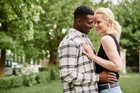 A happy African American man and Caucasian woman standing closely together in a vibrant park, showcasing love and unity.