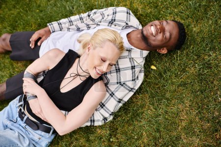 A multicultural couple, an African American man and a Caucasian woman, laying on a grass in park.