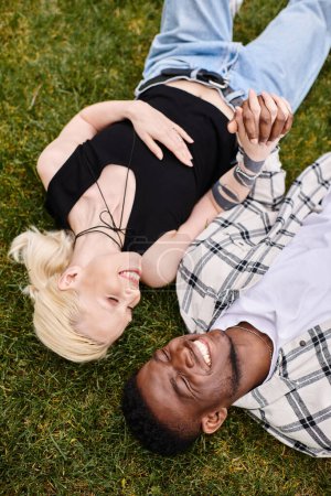 Ein glückliches, multikulturelles Paar, ein afroamerikanischer Mann und eine kaukasische Frau, entspannen sich gemeinsam und umarmen sich auf sattgrünem Gras in einem Park.