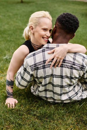 A happy multicultural couple, an African American man and a Caucasian woman, sharing a tender hug on the grass in a park.