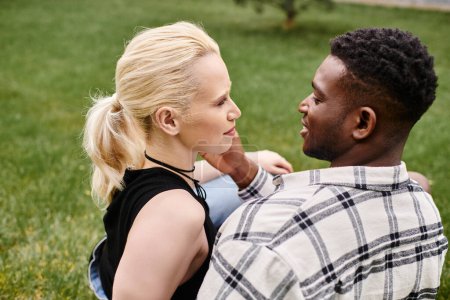 Ein glückliches multikulturelles Paar, ein afroamerikanischer Mann und eine kaukasische Frau, sitzen im Gras eines Parks.