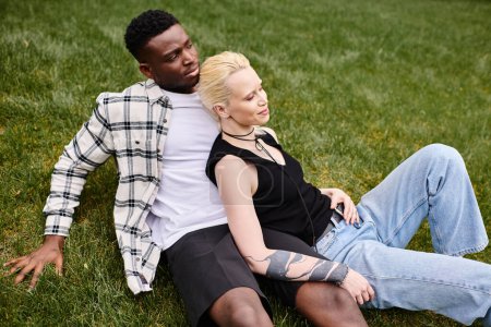 A multicultural couple, an African American man, and a Caucasian woman, laying contently on the grass in a park.
