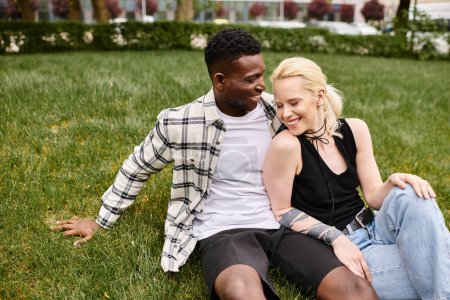 Ein glückliches, multikulturelles Paar, bestehend aus einem afroamerikanischen Mann und einer kaukasischen Frau, sitzt im Gras eines Parks.