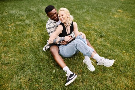 A happy African American man and Caucasian woman sitting peacefully together on the green grass in a park.