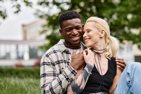 Multikulturelles Paar, ein afroamerikanischer Mann und eine kaukasische Frau, sitzen glücklich zusammen im Gras eines Parks.