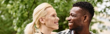 Un hombre afroamericano feliz está al lado de una mujer rubia al aire libre en un parque, sonriendo y conectando.