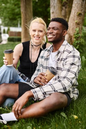 A multicultural couple, an African American man and a Caucasian woman, sit together in the lush green grass of a park.